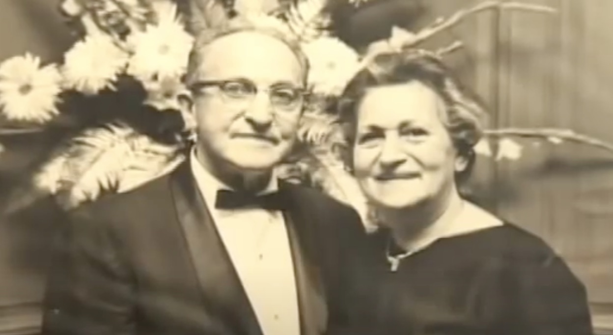 A photograph of Abe and Fannie Birenbaum in front of a bouquet of flowers. Abe is wearing a tuxedo and Fannie is wearing a black dress.